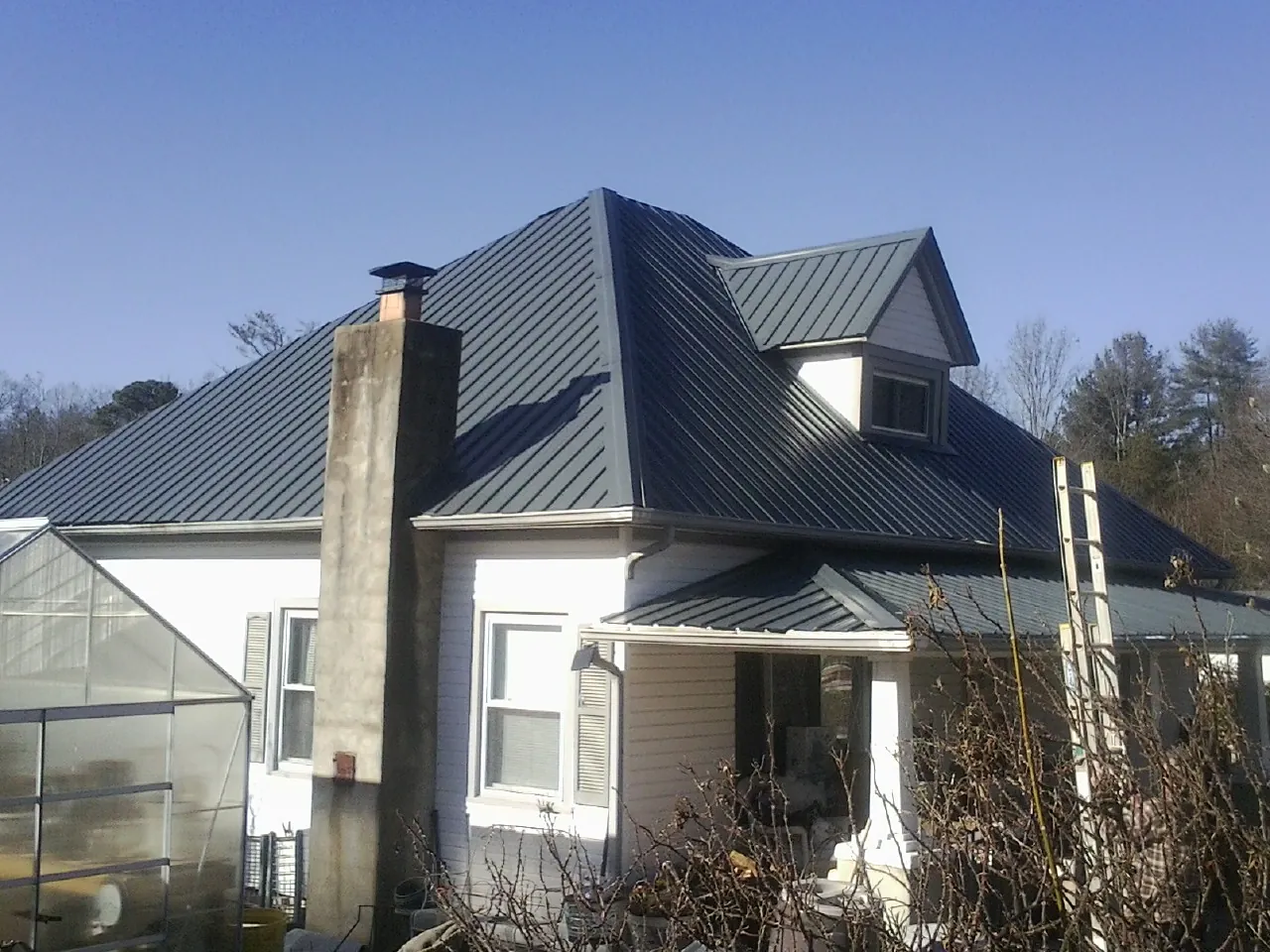 Dark blue standing seam metal roof on a white farmhouse with dormer — Slate & Tile Roof Repair by Roofing Brothers in Ravenswood