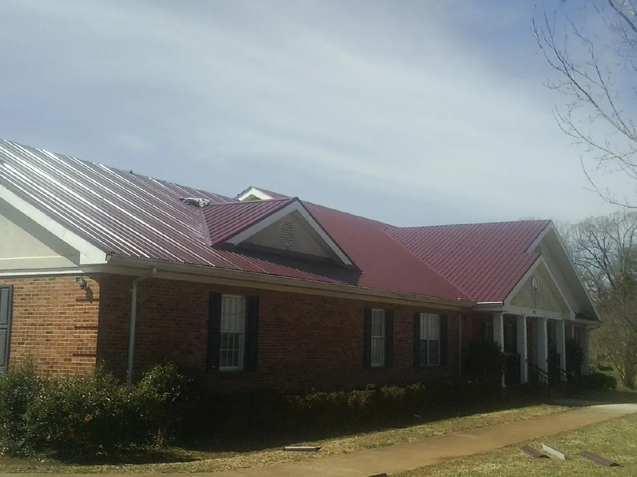 Red metal roof with gabled entries on a long brick building, from a Hail Damage Roof Repair job in Ravenswood
