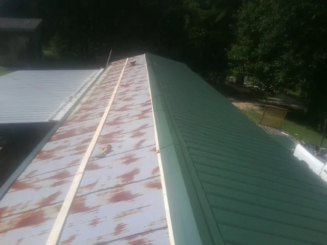 Old rusted panels beside newly installed green metal roofing — Wind Damage Roof Repair by Roofing Brothers in Ravenswood