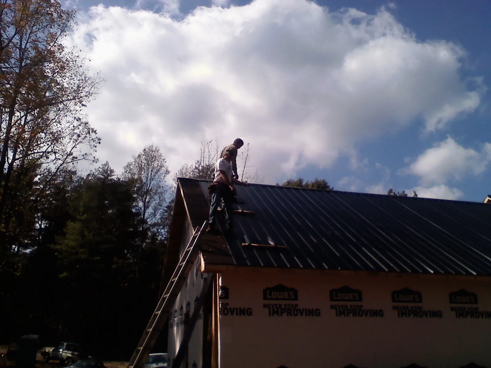 Roofer fastening dark metal panels high against a cloudy sky, from a Roof Inspection job in Ravenswood