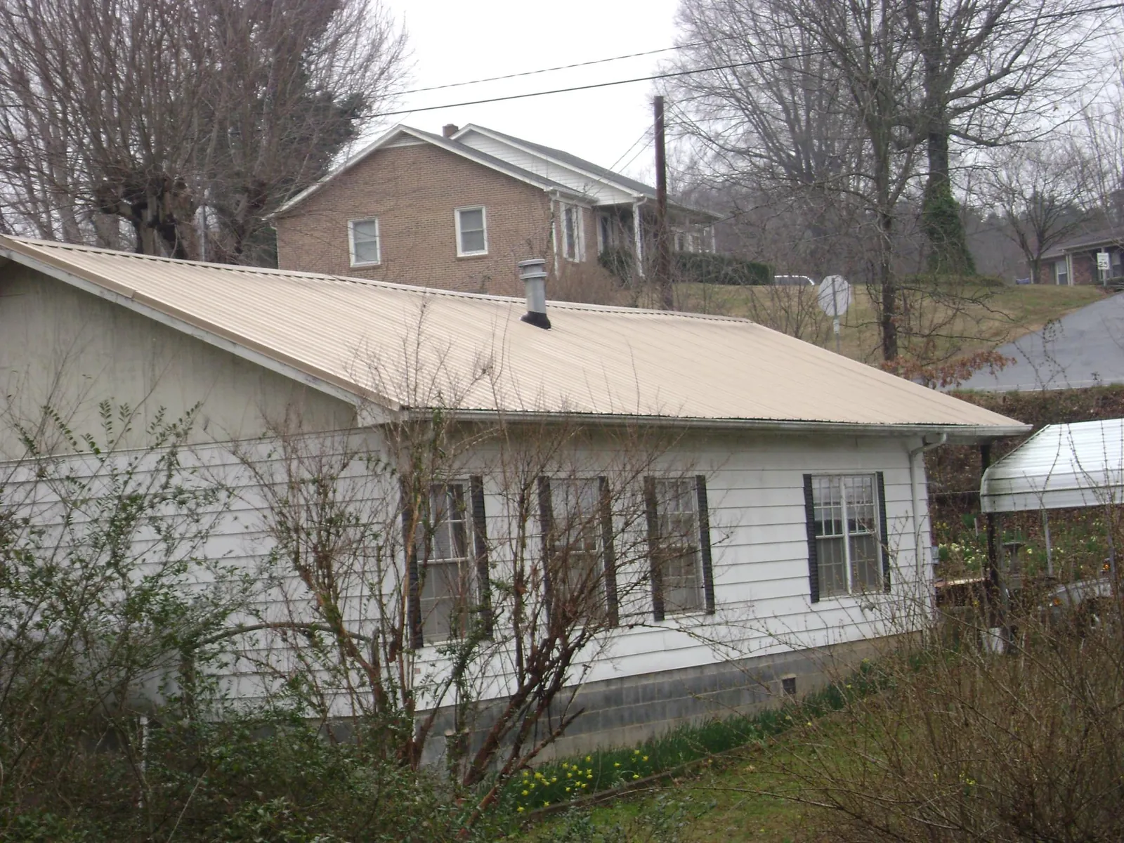Tan metal roof on a white sided house set into a hillside — Commercial Roofing by Roofing Brothers in Ravenswood
